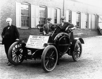 a black and white photo of Thomas Edison standing next to a car