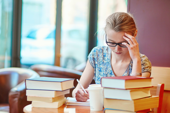 a girl sitting at a table with a pile of books in front of her