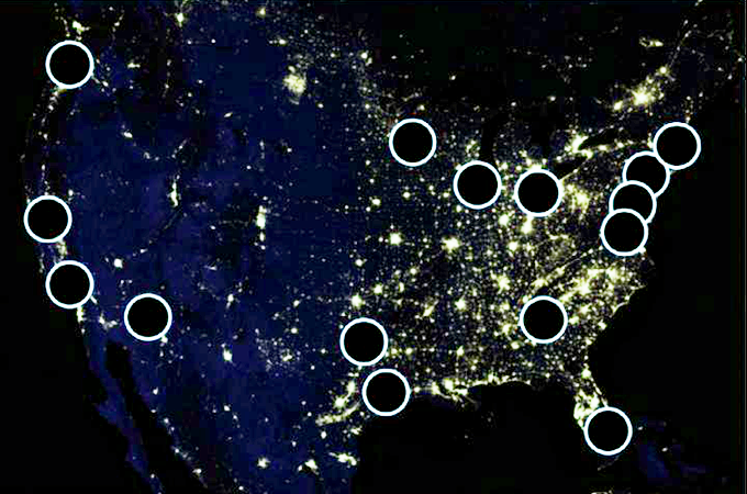 An image of the United States at night from orbit with areas of high population showing as bright clusters of light. There are fifteen black circles outlined in white representing the 15 largest U.S. metro areas.