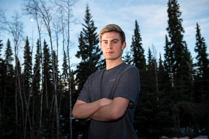 A photo of Nathan Baring standing outside in front of tall narrow evergreen trees.