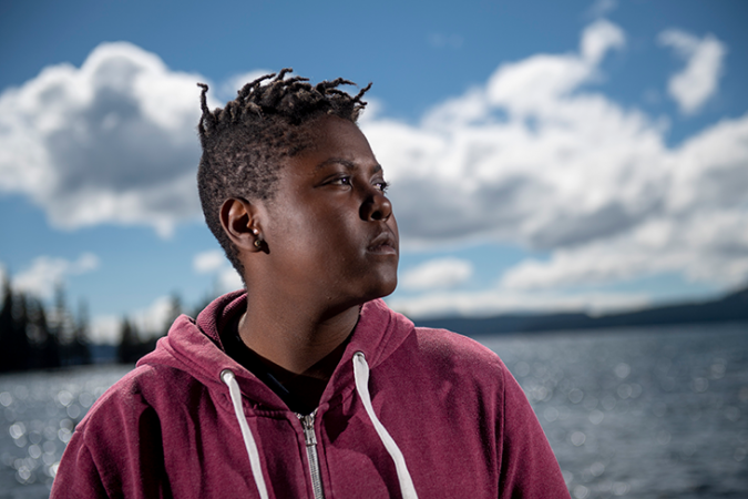 A photo of Vic Barrett standing in front of a body of water on a sunny day. She is looking to her left.