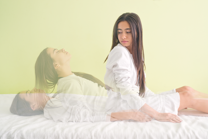 A sitting woman looks down at her dreaming self