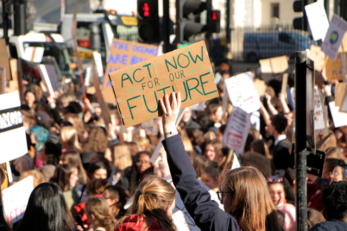 A photo of a climate strike march in London.  A sign held over the protesting throng reads "Act now for the future."