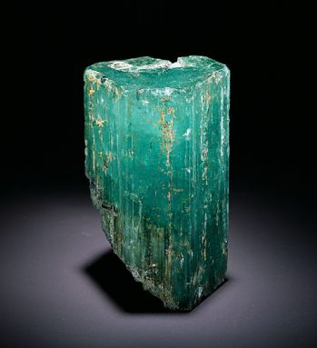 a photo of an unpolished emerald agains a black background