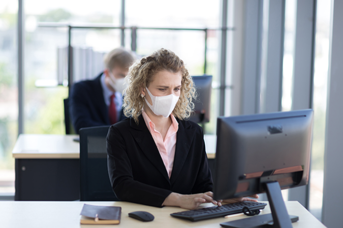 a photo of a lady working at a computer wearing a face mask in an office setting