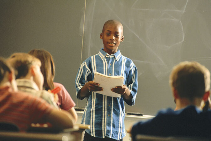 a boy gives a speeh in front of a classroom