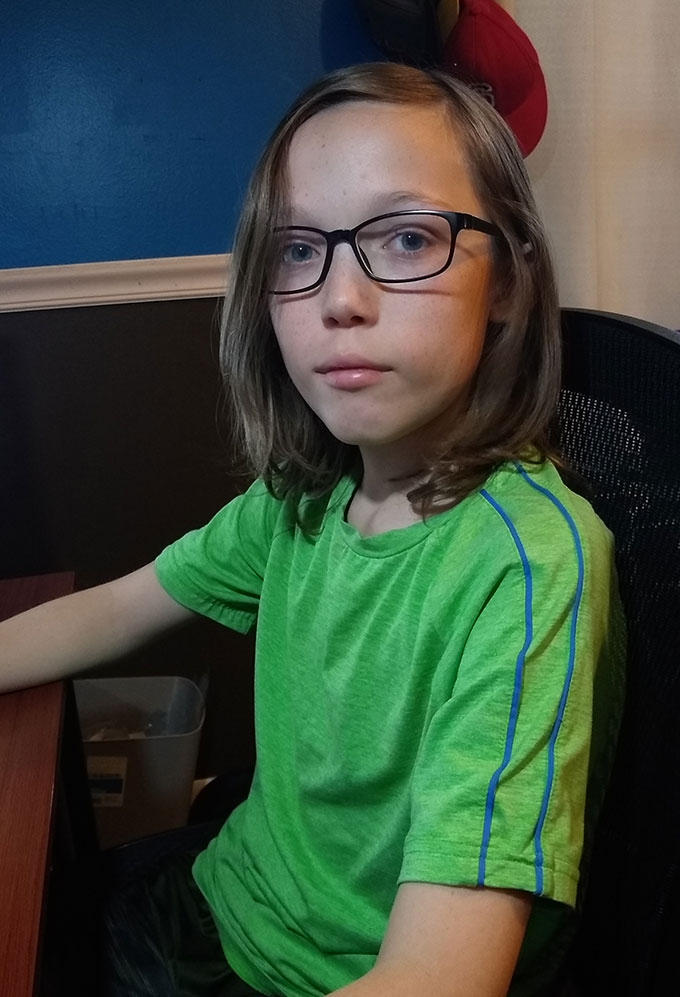 a photo of Spencer a 12 year old boy wearing a green shirt and glasses sitting at a desk