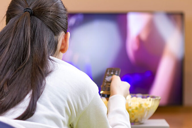 a photo of the back of the head of a girl watching TV with a bowl of popcorn