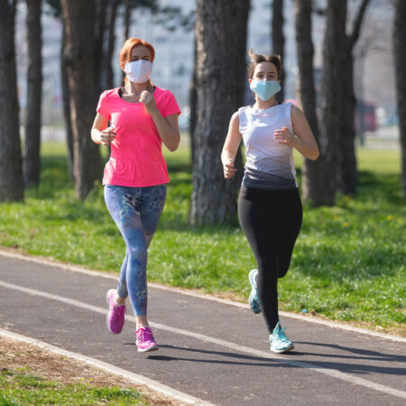a photo of two women running on a track wearing face masks