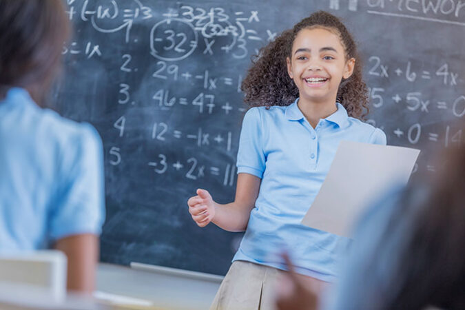 an girl standing in front of a chalkboard full of equations and smiling