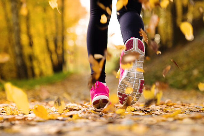 a photo of a person running away from the viewer on a leafy path, zoomed in on the feet and lower legs 