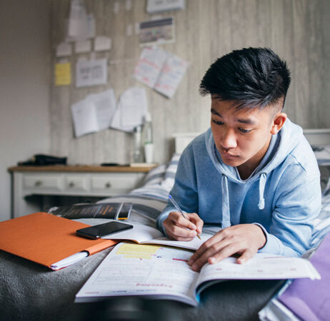 снимка на млад азиатски мъж, който изучава бележките си, докато лежи в леглото