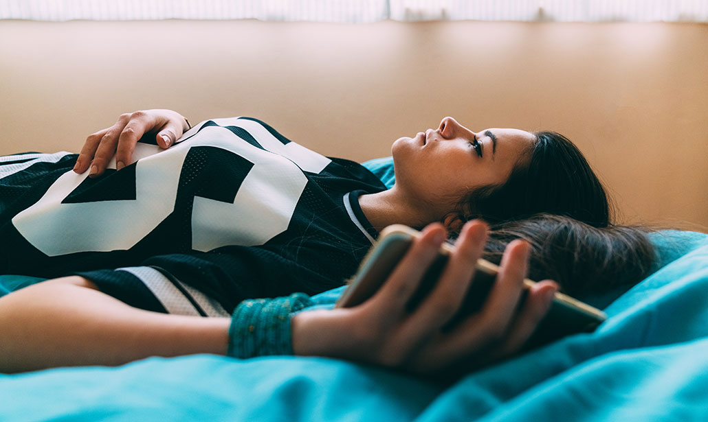 a young woman lying on her bed looking at the ceiling with a phone in her hand