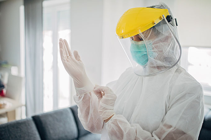 a photo of a woman wearing PPE and putting her hands in surgical gloves