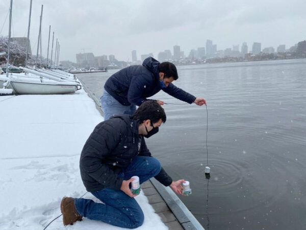 two men placing a sensor in a river on a snowy day
