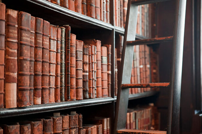 a bookshelf full of old books in brown leather binding, there is a library ladder next to the shelf