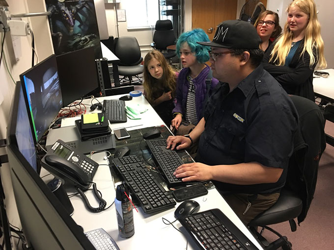 a man sitting at a desk playing video games with four onlookers