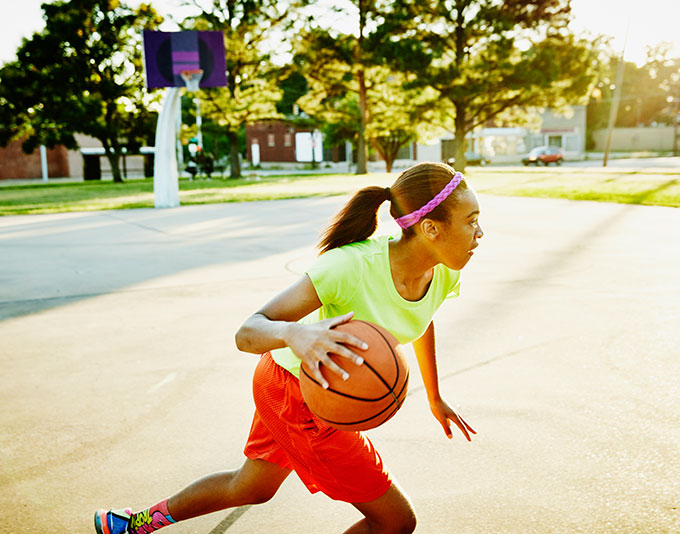 a girtl dribbling a basketball on an outside court