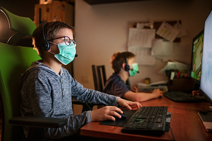 two boys wearing face masks and playing computer games