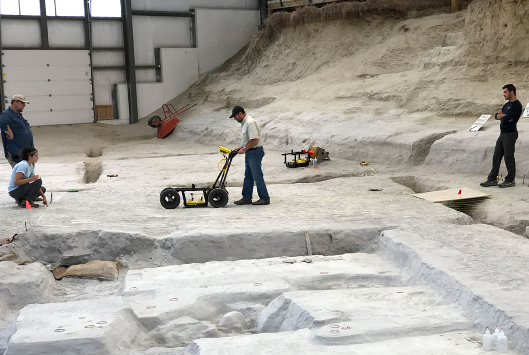 Researchers pushing a ground-penetrating radar machine over the ground.