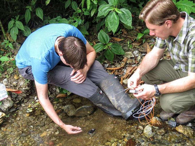 two men in and next to a creek doing field research