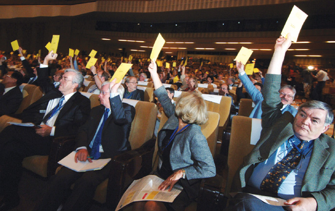 members of the International Astronomical Union hold up yellow cards to vote in an auditorium