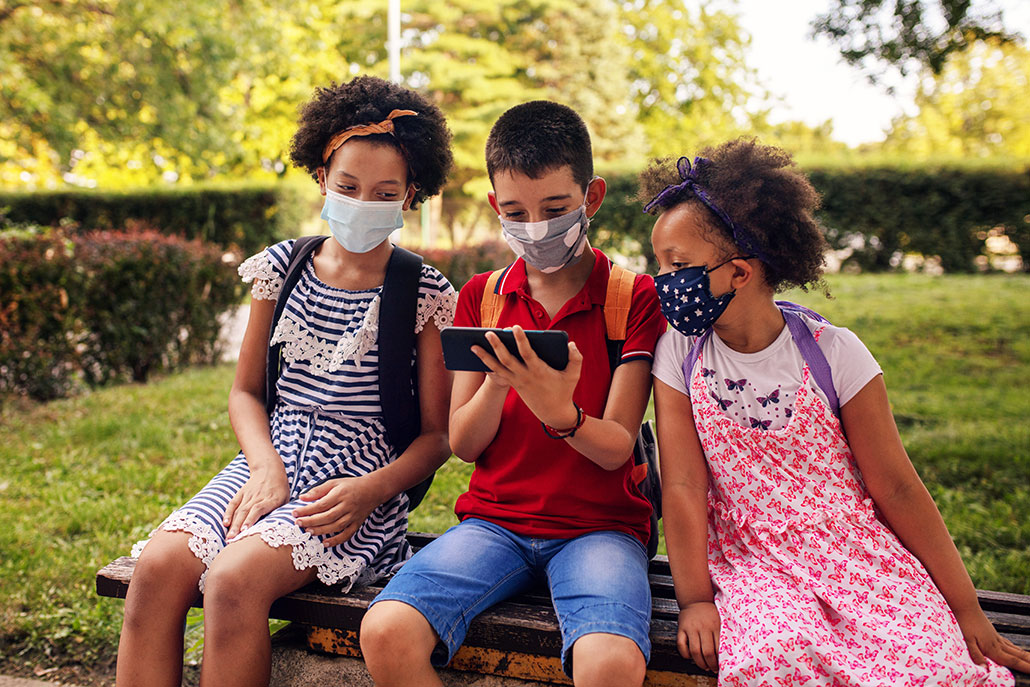 three masked student friends sitting together outside and looking at phone together