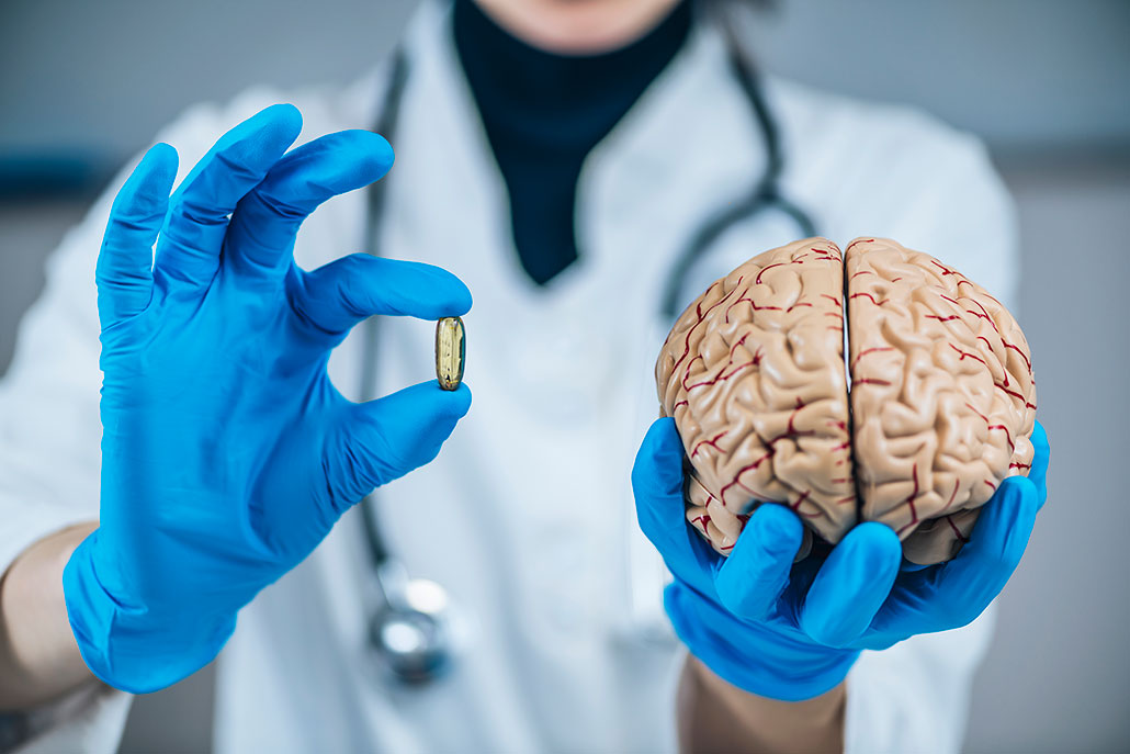 a scientist holds up a pill and a model of the human brain