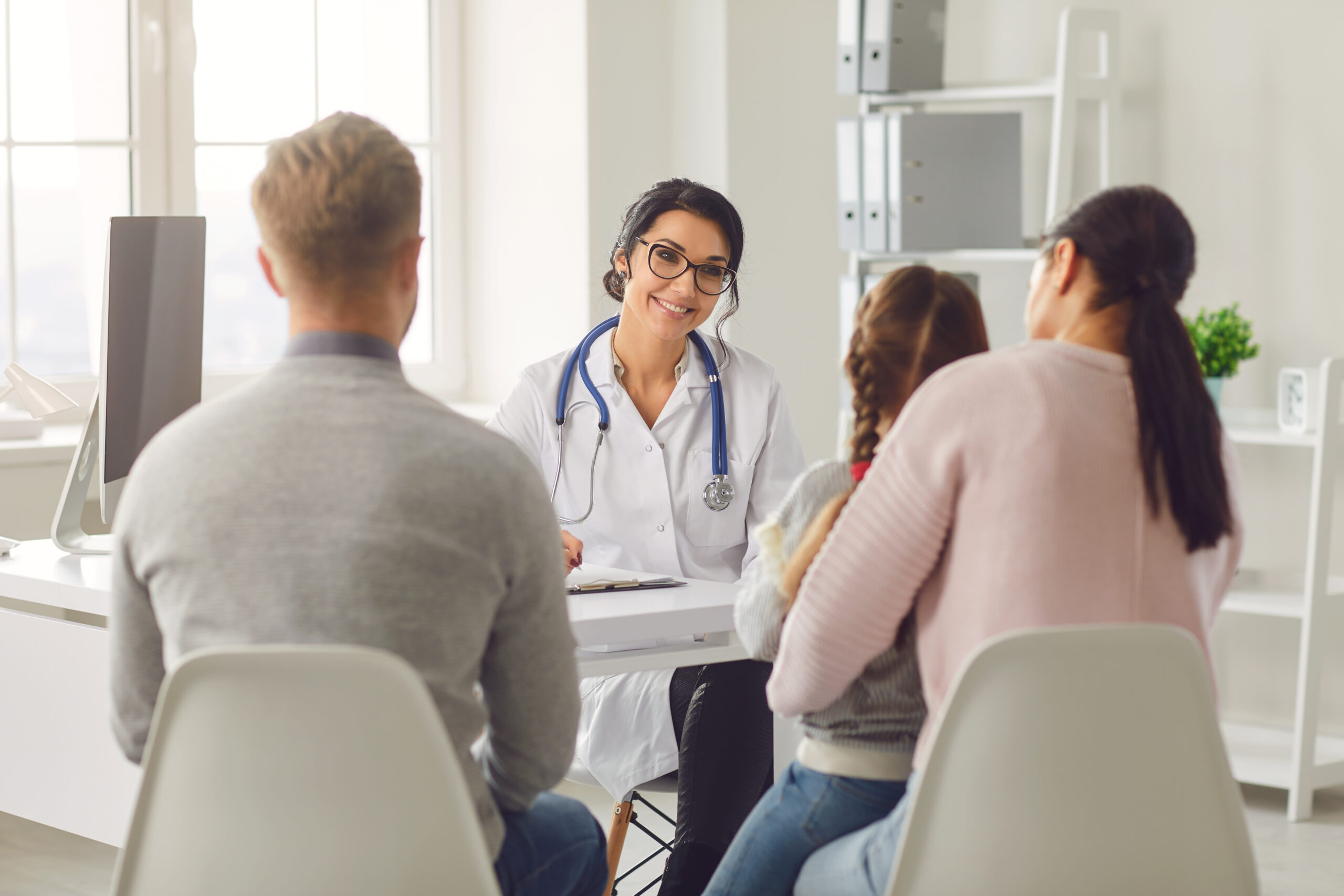 a child sits on her parents lap as they talk to a smiling female doctor across a desk