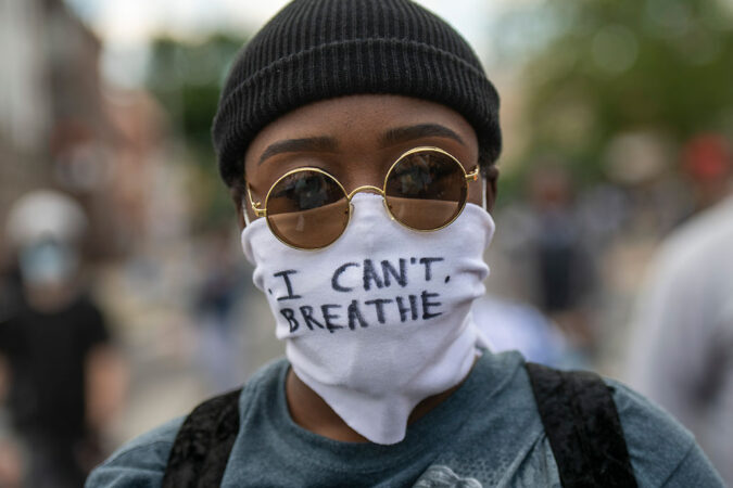 A Black protester wearing a hat, sunglasses, and a mask that has "I CAN'T BREATHE" written on it