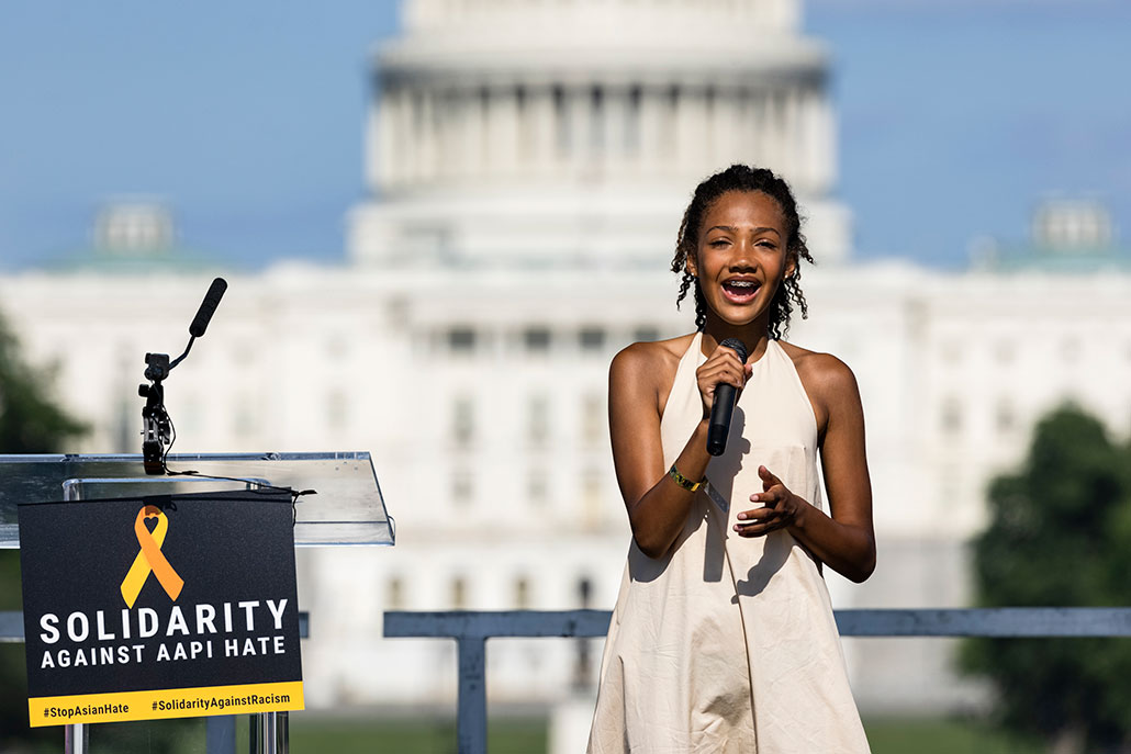 a photo of Tatum Francois, a young black woman with braids wearing a dress, holding a microphone and singing