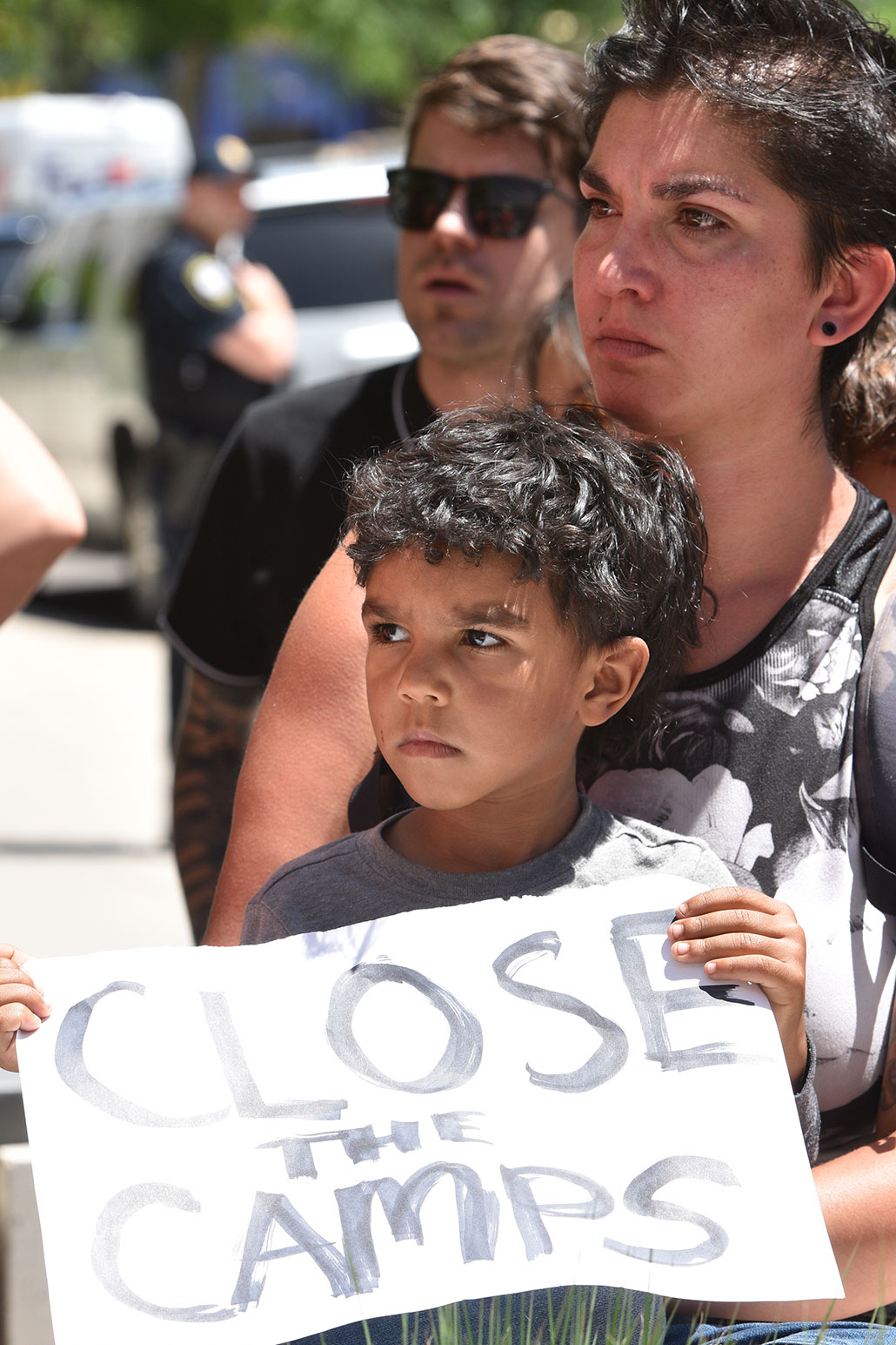 a boy and his mother at a protest. The boy is holding a sign that says "Close the Camps"