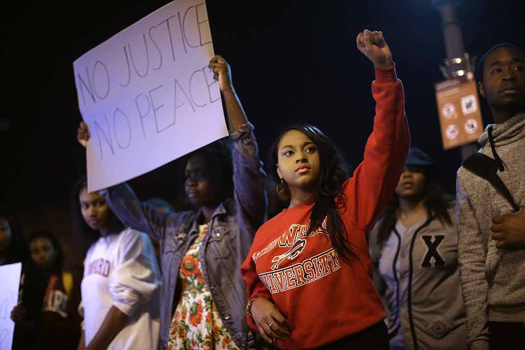 a photo of black teens at a nighttime protest one girl holds a sign that reads "No Justice, No Peace"
