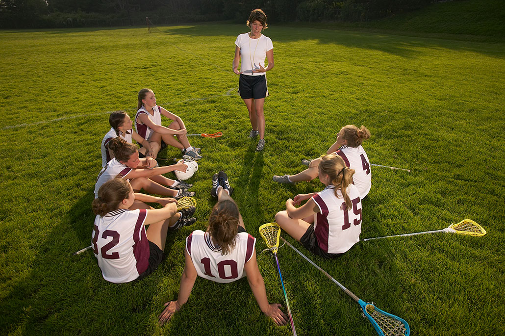 a ring of women lacrosse players listens to a coach