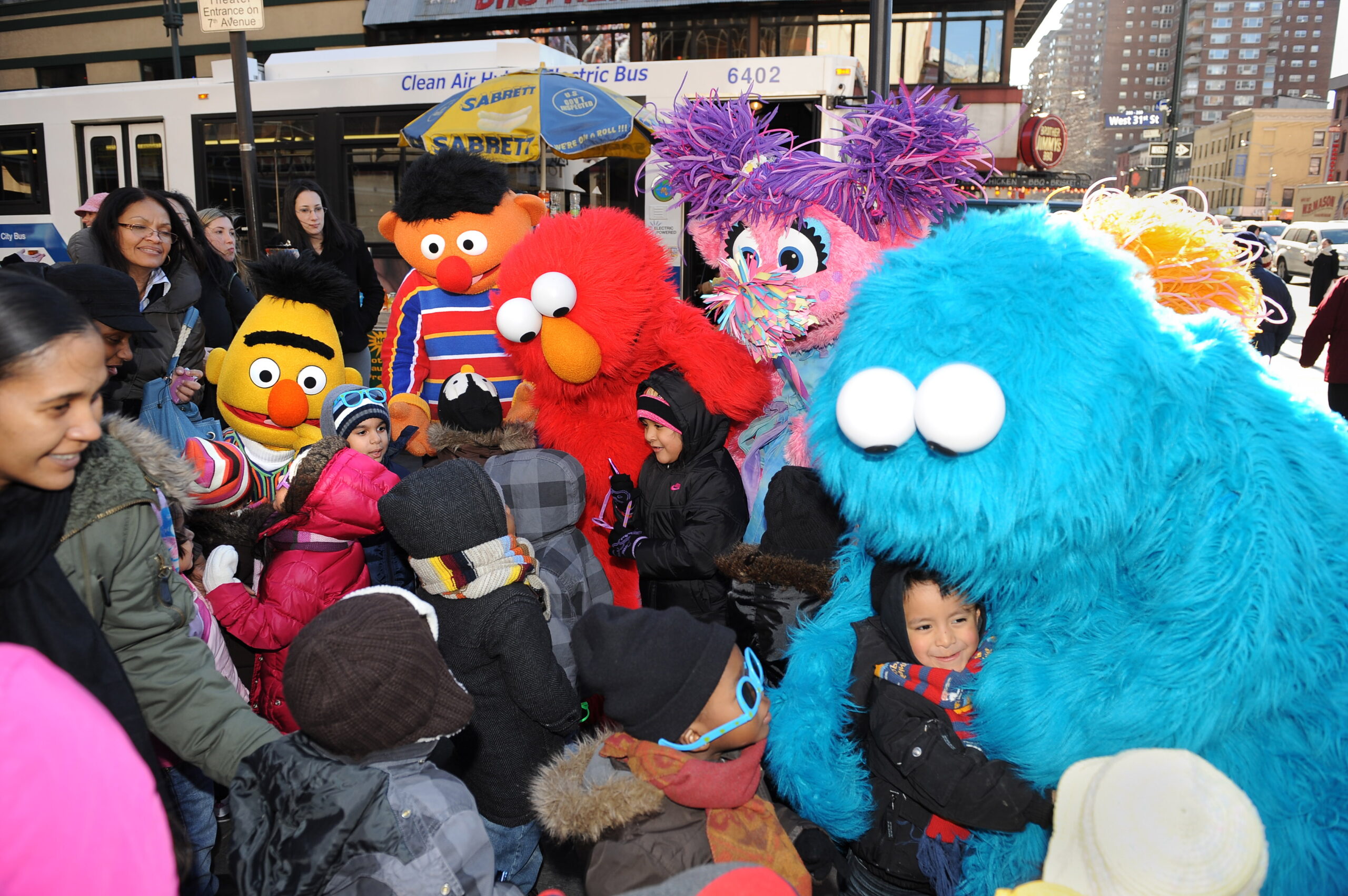 a crowd of children take pictures with people wearing Elmo, Cookie Monster and other Sesame Street character costumes