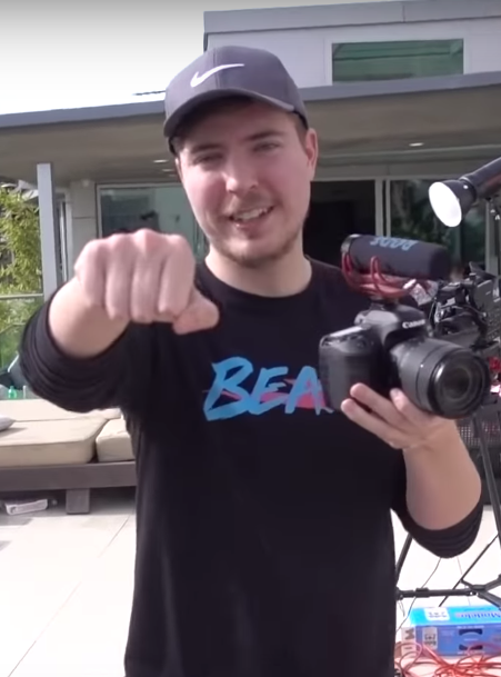 The youTuber MrBeast, wearing a black shirt and ball cap, holds out a fist -- as if asking for a fist bump -- to the camera