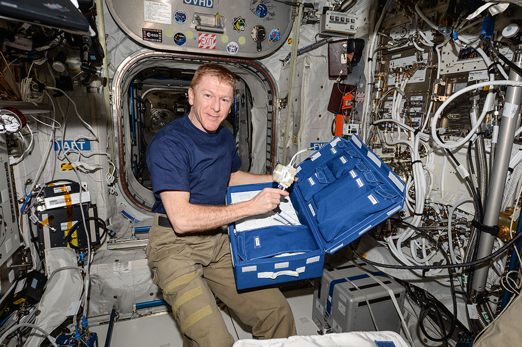 a photo of a male astronaut holding a measuring device while floating in the International Space Station