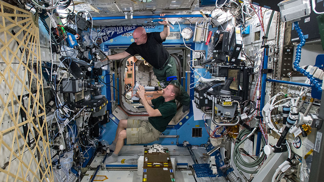 a photo of two male astronauts doing eye exams while floating inside the International Space Station