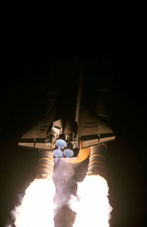 a photo of a nighttime launch of the space shuttle Discovery. The back of the shuttle is lit up by the exhaust from the rockets 