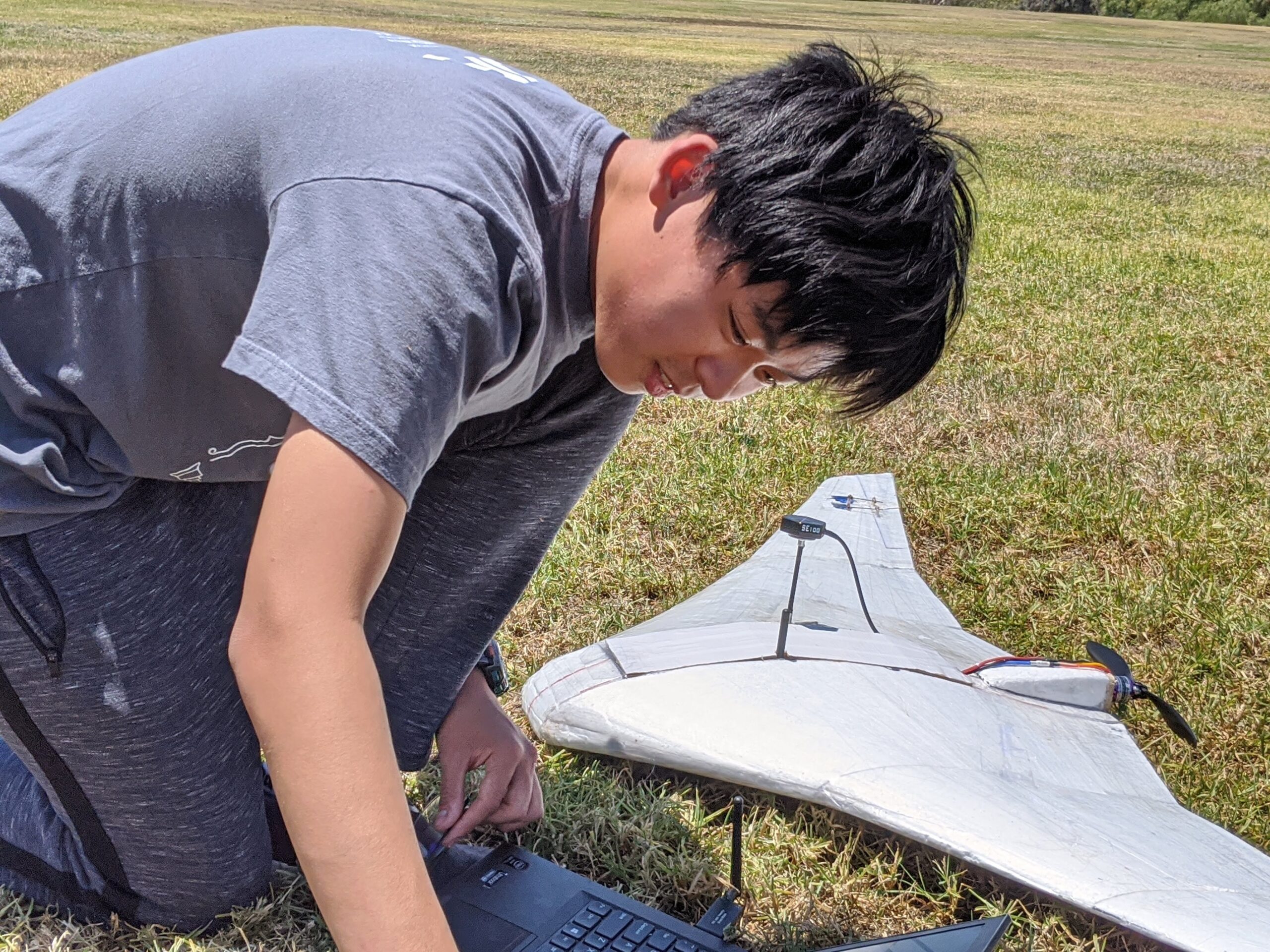 a boy crouches in the grass on a sunny day beside a white model airplane 