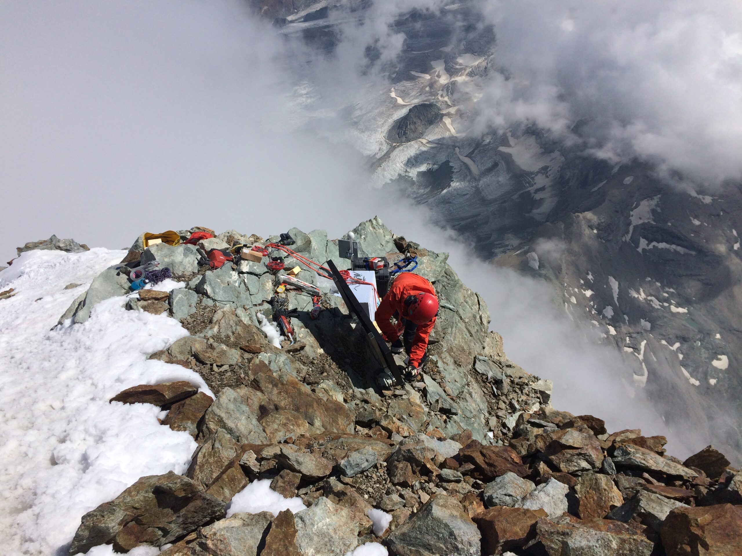 a photo looking down at Samuel Weber installing a seisometer on a rocky outcropping