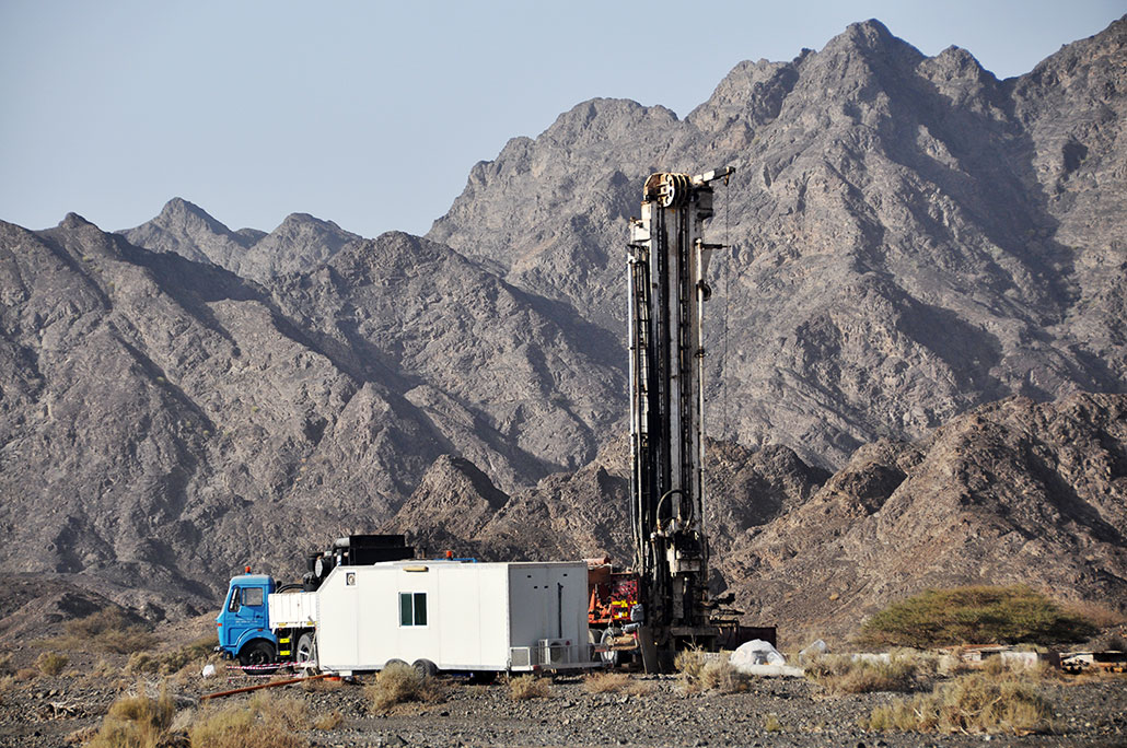 a photo of a drilling site in Oman. There are mountains in the distance.