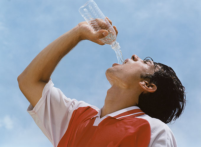 a sweaty man in a sports uniform is drinking water from a plastic water bottle