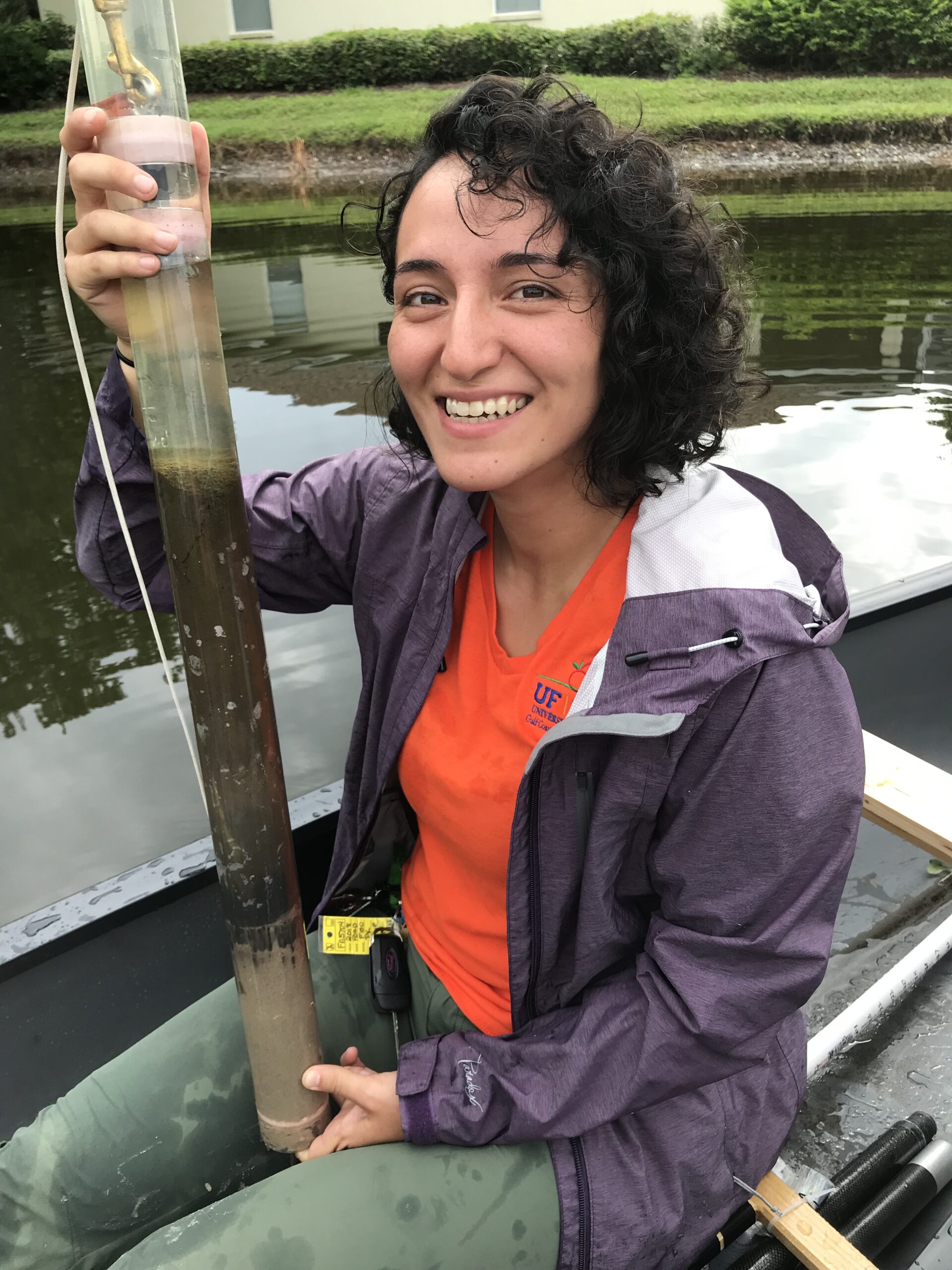 a woman poses in a canoe holding a tall tube filled with sediment