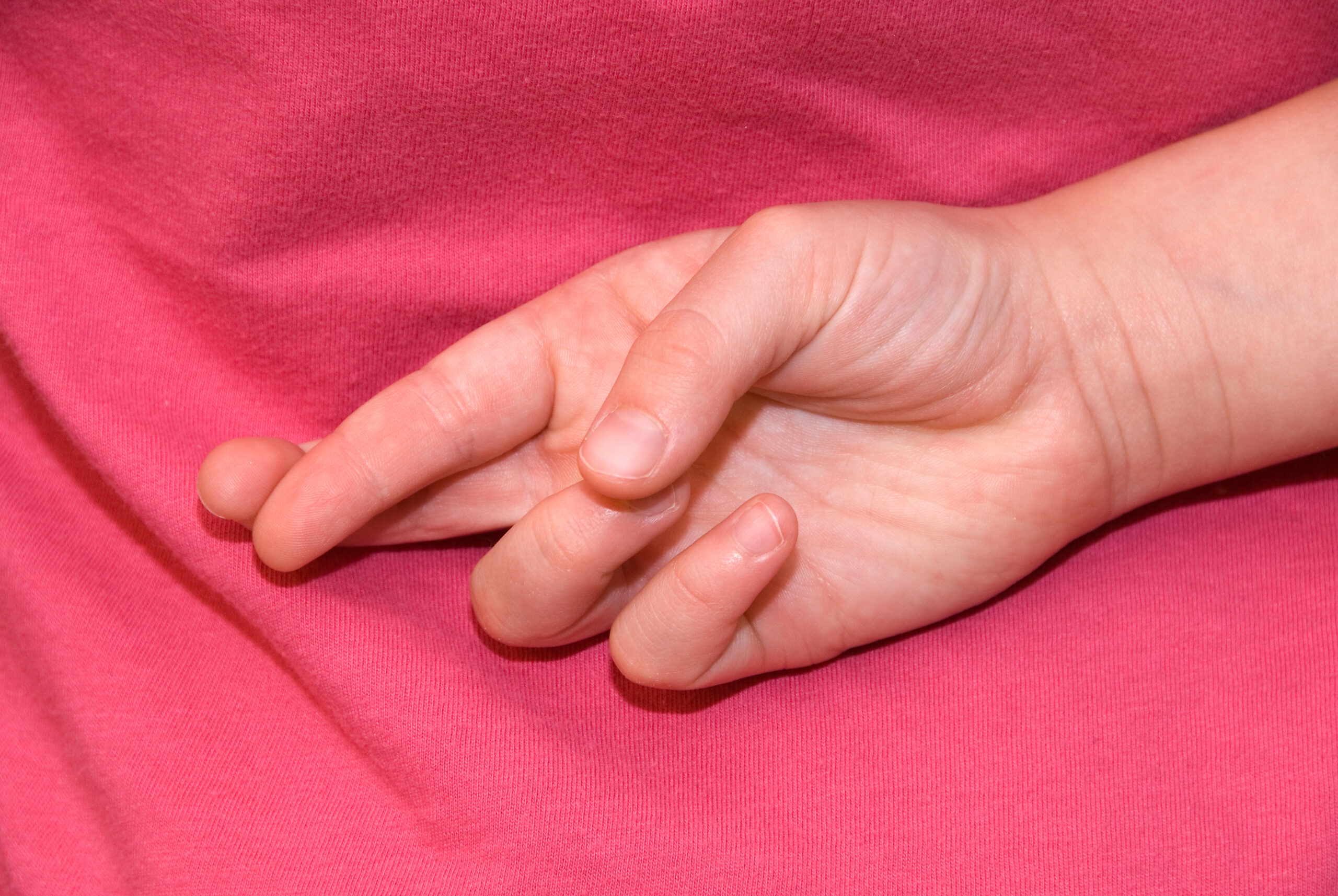 a hand crosses its middle and forefingers against a pink cloth backdrop
