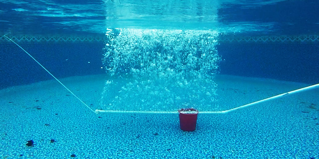 an underwater view of a pool shows a curtain of bubbles emitted by a pipe rising toward the surface