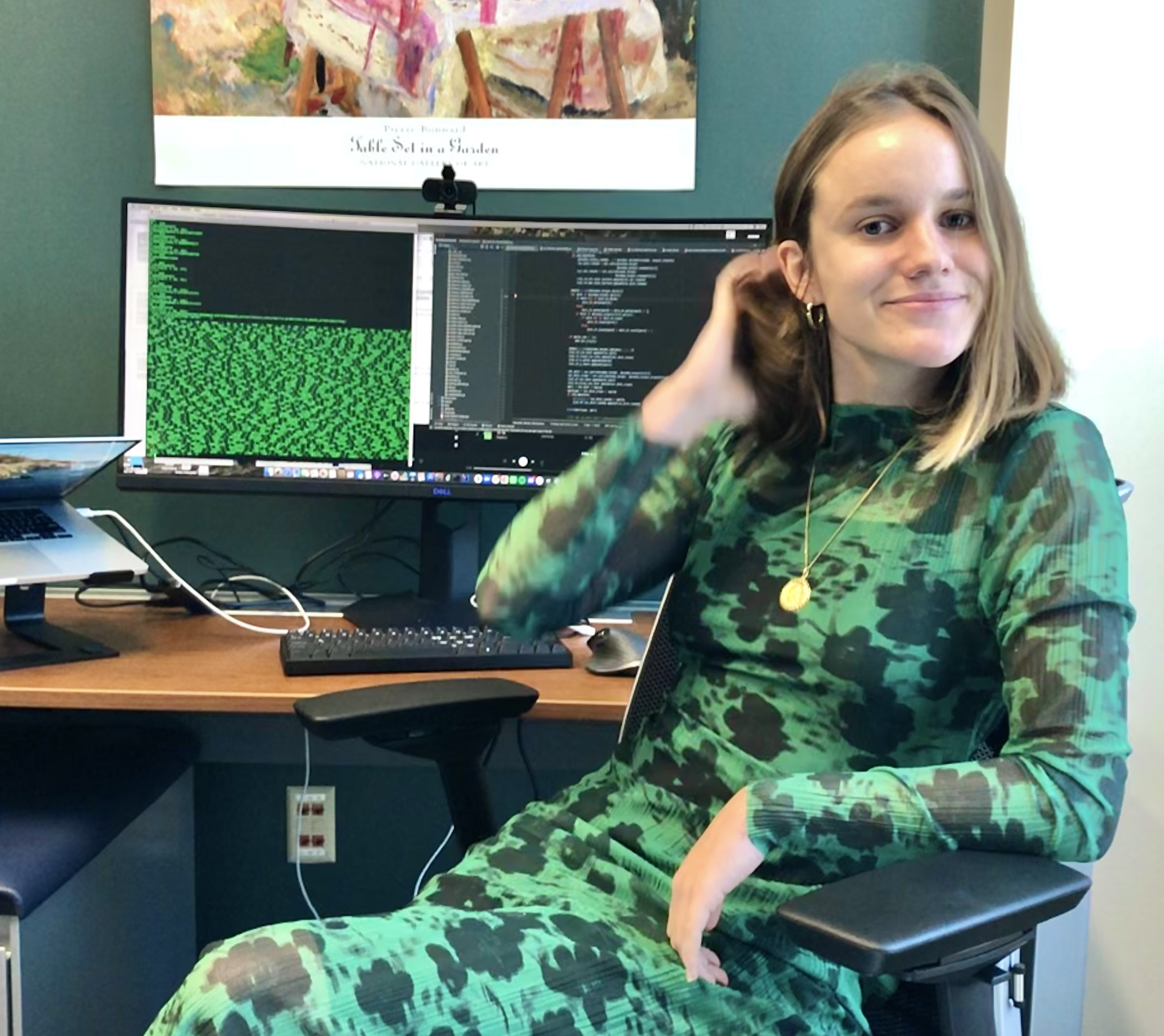 a woman in a black and green dress sits at a desk with a computer