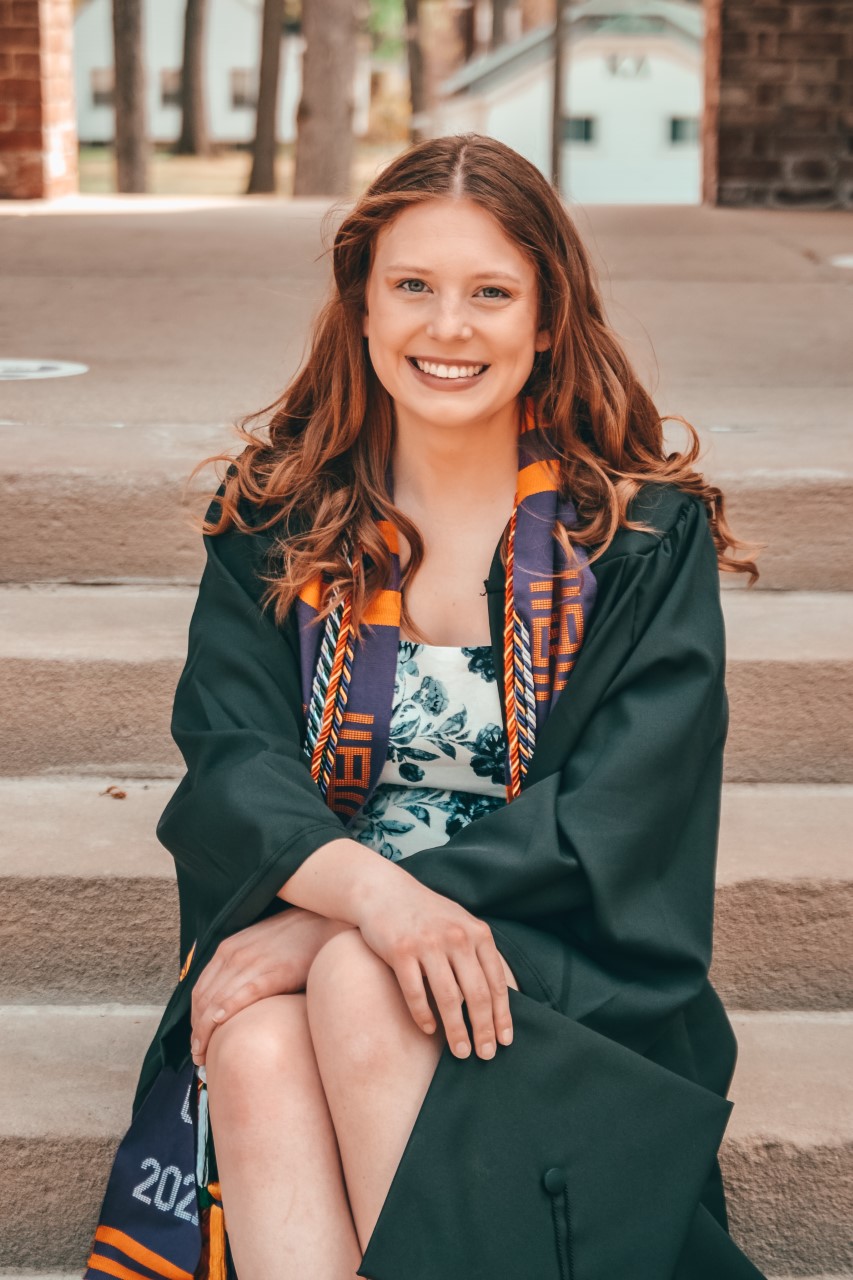 a smiling girl wearing a green graduation gown sits on a staircase outdoors