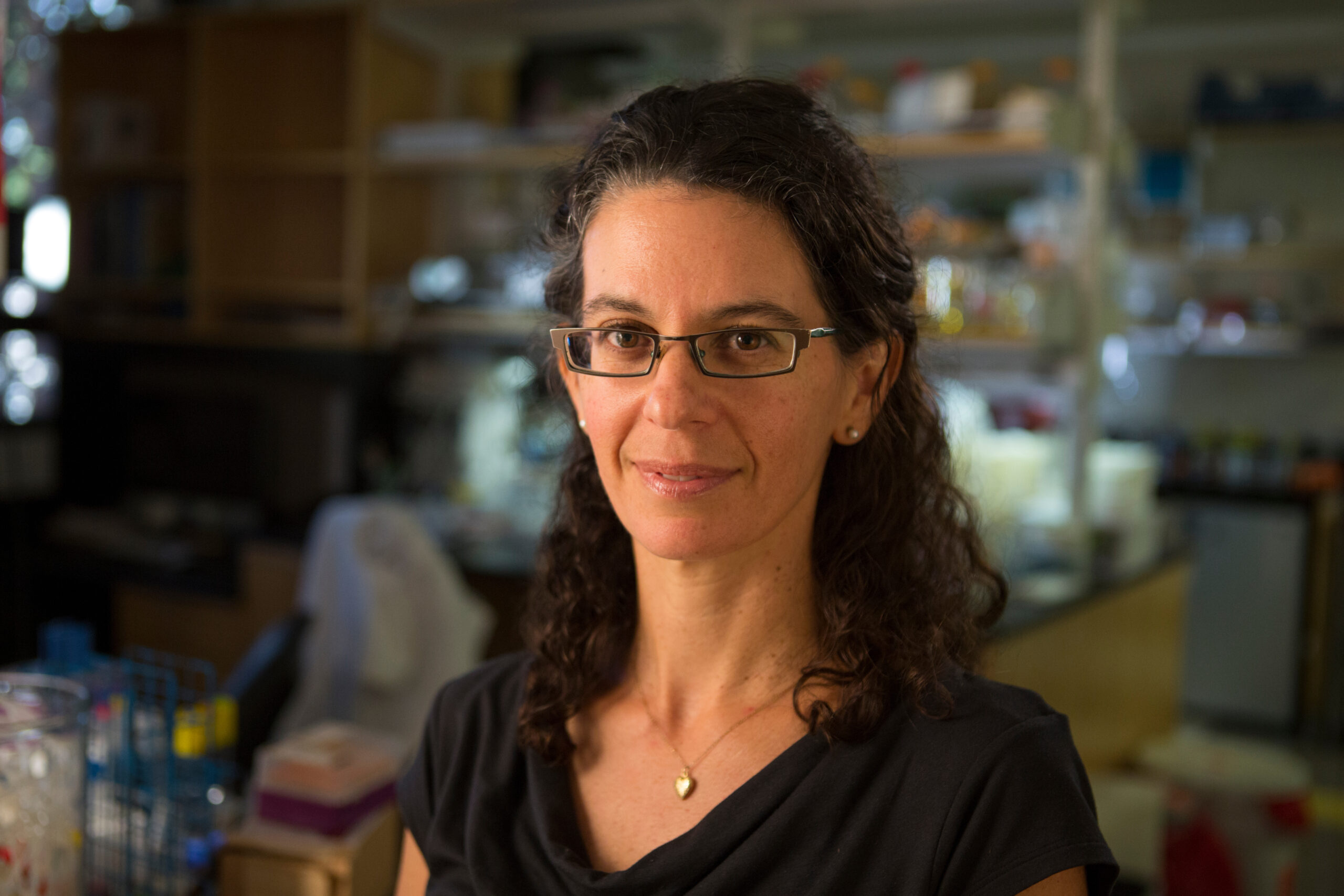 A smiling brunette woman wearing glasses stands in a science lab